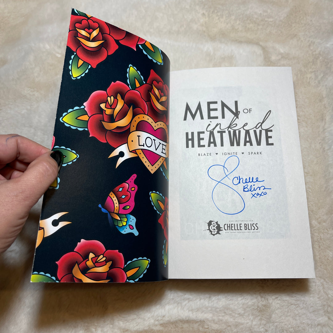 Men of Inked Heatwave Volume 2 paperback book opened to the title page, displaying a Chelle Bliss autograph.