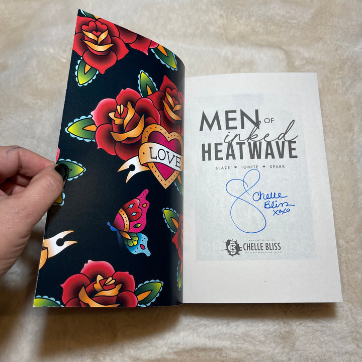 Men of Inked Heatwave Volume 2 paperback book opened to the title page, displaying a Chelle Bliss autograph.