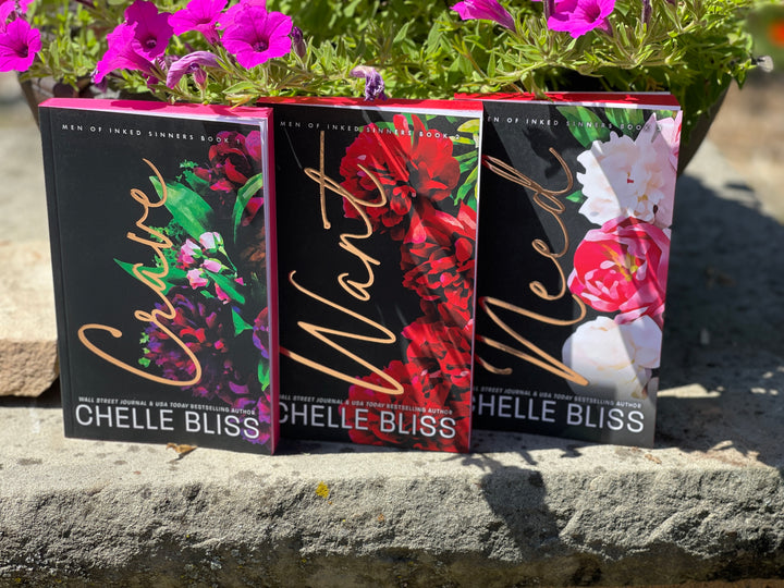 Three books by Chelle Bliss, Crave, Want and Need on a stone ledge with flowers in the background