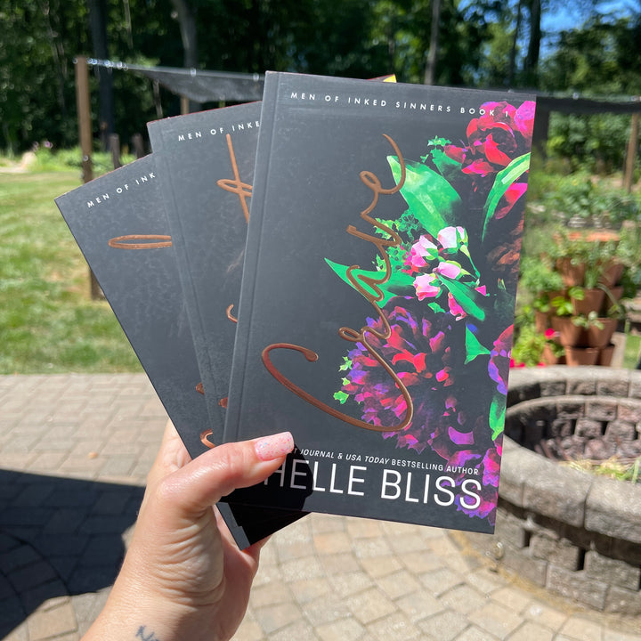 Three books, Crave, Need and Want held by a hand with a garden background