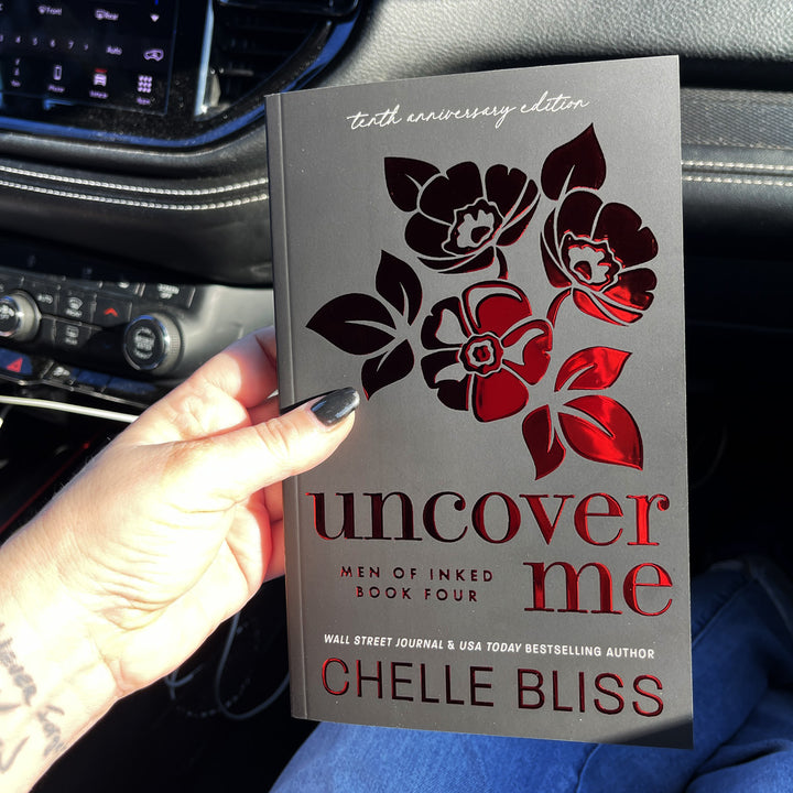 paperback book Uncover Me 10th Anniversary Foil Special Edition by Chelle Bliss with red flowers on the cove held in a hand in a vehicle.